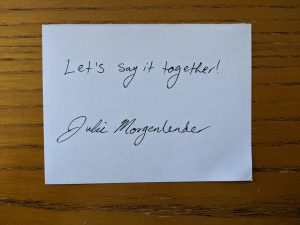 White cardwith text "Let's say it together!" and signature beneath text.
